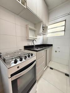 a white kitchen with a stove and a sink at Pé na Areia Praia do Gonzaguinha II in São Vicente