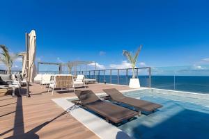 a swimming pool with chaise lounge chairs and the ocean at ART STUDIO VISTA Mar FRONTAL ARMAÇAO PITUBA in Salvador