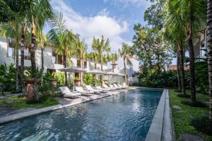 a swimming pool with chairs and umbrellas and palm trees at Anam Tang New Rooms & Cafe near Seminyak in Seminyak
