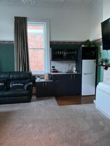 a living room with a black leather couch and a kitchen at Sahara Guest House in Dunedin