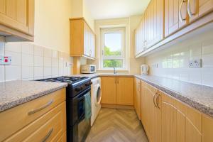 een keuken met houten kasten en een kookplaat met oven bij Walk to Hydro and SEC Modern 3BR Free Parking in Glasgow