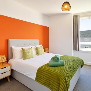 een slaapkamer met een groot bed met een oranje muur bij Walk to Hydro and SEC Modern 3BR Free Parking in Glasgow