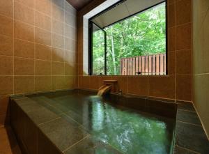 a bath tub with a window in a room with water at  Hakkai Konohanakan in Oshino