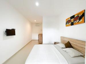 a white bedroom with a bed and a tv on the wall at Urbanview Hotel Lilis Ikvala Radha in Canggu