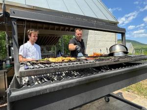 two men standing next to a grill with food on it at Csernus Doki bor-grillterasza és bungallói in Eger