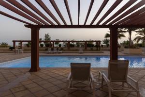 zwei Stühle unter einer Pergola neben einem Swimmingpool in der Unterkunft Shomoukh - شموخ in King Abdullah Economic City