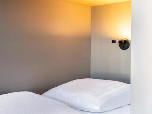 a bedroom with two white beds and a light on the wall at B&B HOTEL Flensburg-City in Flensburg