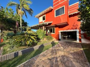 une maison rouge avec une allée et un palmier dans l'établissement CASA PINHEIROS - Casa na Praia de Palmas com 4 Dormitórios e Piscina, à Governador Celso Ramos