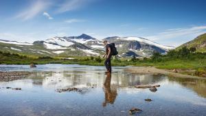 Ein Mann geht über einen Fluss mit schneebedeckten Bergen in der Unterkunft Breifossen hytteutleie in Namsskogan