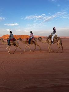 three people riding on camels in the desert at DESERT BREATHS lUXURY CAMP in Wadi Rum