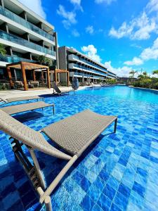 a swimming pool with lounge chairs in front of a building at Luxuoso e sofisticado Beach Class Summer by HM in Porto De Galinhas