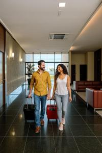a man and woman walking down a hallway with luggage at Flat Blue Praia de Camburi in Vitória +82 photos