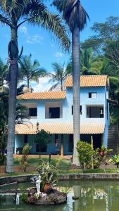a house with palm trees in front of a body of water at Chacara da Cachoeira Waterfall Farm in Caratinga