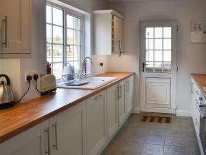 a kitchen with white cabinets and a sink and a door at Bramble Cottage in Craster