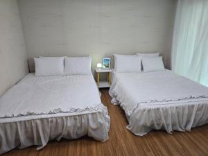 two beds in a room with white walls and wood floors at Yeoncho Money Stay in Geoje 