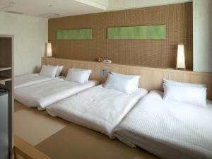 three beds in a room with white sheets and pillows at Hotel Nikko Narita in Narita