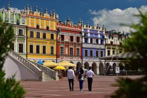 three people walking down a street in front of buildings at Nook Apartment Zamość Old Town in Zamość