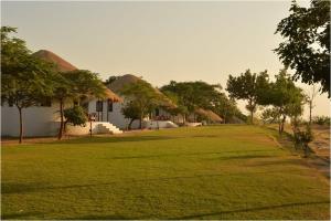 a row of huts with trees and a grass field at Kutch Safari Resort in Kunria