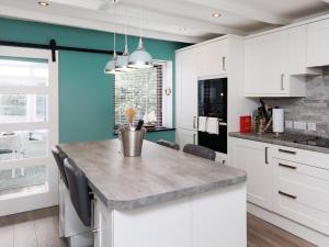 a kitchen with white cabinets and a blue wall at Weavers Cottage in Back
