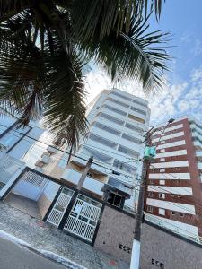 a tall building with a palm tree in front of it at Pé na Areia Praia do Caiçara in Solemar