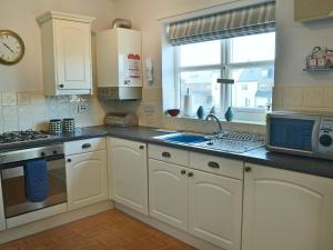 a kitchen with white cabinets and a sink and a microwave at Captain Ron's in Beadnell