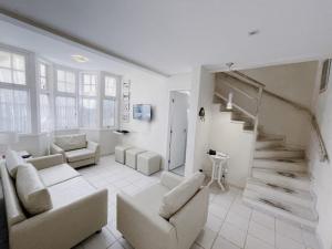 a living room with white furniture and a staircase at Home 80 I Casa em condomínio pé na areia em Juquehy WIFI e Piscina in São Sebastião