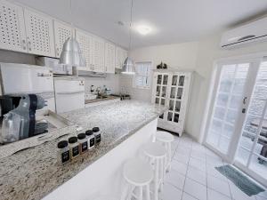 a white kitchen with white appliances and stools at Home 80 I Casa em condomínio pé na areia em Juquehy WIFI e Piscina in São Sebastião