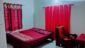 a bedroom with red curtains and a bed and a chair at Devadeyam homestay in Pūvār
