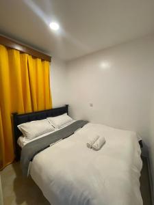 a bedroom with a bed with white sheets and yellow curtains at Cozy Kipepeo Cottage in Nairobi