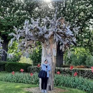 Una mujer parada frente a un árbol con una escultura de pájaro. en A private room in a flat shared familly home, en Mulhouse