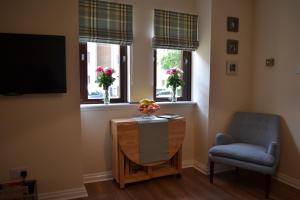 a living room with a table and a chair and two windows at Boat Green Apartment in Edinburgh
