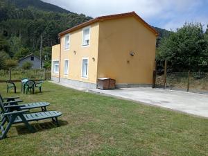 a yellow building with picnic tables and benches in the grass at Casa independiente Solana in O Lourido