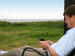 a man sitting in a chair looking at a cell phone at 8 person holiday home in Nysted-By Traum in Nysted