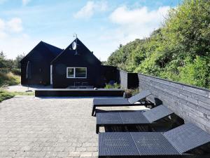 a black house with a stone wall and two benches at 5 star holiday home in Blokhus in Blokhus