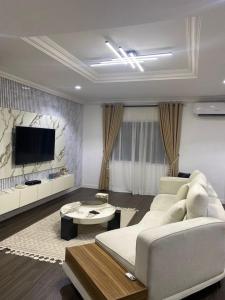 Il comprend un salon doté d'un mobilier blanc et d'une télévision à écran plat. dans l'établissement synergy Smart luxury Apartment, à Ikeja