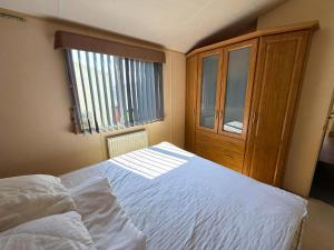 a bedroom with a white bed and a wooden cabinet at Lovely Caravan With Wifi & Decking At Felixstowe Beach Holiday Park Ref 55005Sw in Walton +14 photos
