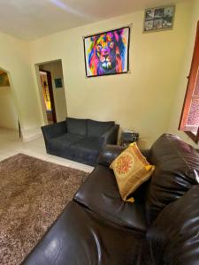 a black leather couch in a living room with a lion painting at Green House Chalé, hostel e pousada in Saquarema