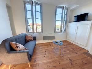 a living room with a blue couch and two windows at Les Arcades - Mirande Centre in Mirande