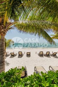 einen Strand mit Liegestühlen und einer Palme in der Unterkunft SEASlDE Beachfront 4 BDR by Casa Paraiso in Cancún