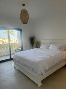 ein weißes Bett in einem Schlafzimmer mit einem großen Fenster in der Unterkunft A Luxurious & Cozy Apartment Greek Village Marassi in El-Alamein