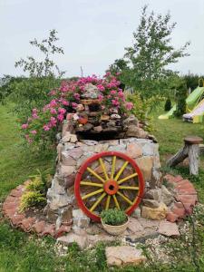 a stone wall with a wooden wheel and pink flowers at Veliki Banjan in Riznica Kraj