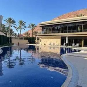 a swimming pool in front of a building with palm trees at Flow - Al Raha Village in Aqaba