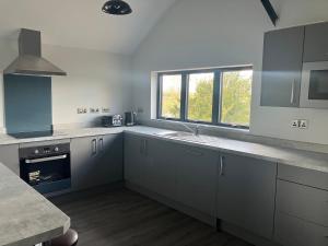 a kitchen with white cabinets and a sink and a window at Stunning Contemporary Dutch Barn Conversion in Whixall