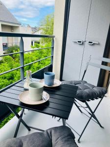 a table with two cups and a chair on a balcony at Appartement Le Cap Trégor Centre Ville in Perros-Guirec