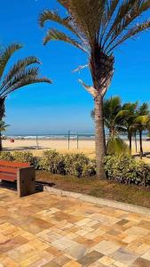 Blick auf einen Strand mit Palmen und einer Bank in der Unterkunft Vista Mar - Kitnet Espaçosa - Tupi in Praia Grande