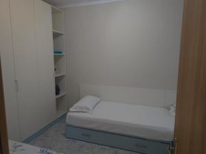 Una pequeña habitación blanca con una cama pequeña y estantes. en Casa di Mare, en Vlorë