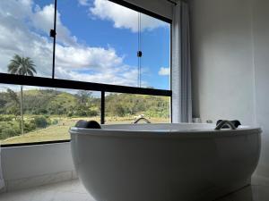 a bath tub in a bathroom with a large window at Aconchego Serrano com banheira in Paty do Alferes +25 photos