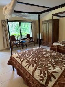 a bedroom with a bed and chairs and a large window at Raja Gardens Hotel in Seminyak