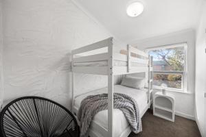 Habitación blanca con litera y silla en Ivy's at Glenelg Central - A Cosy Family Stay, en Glenelg
