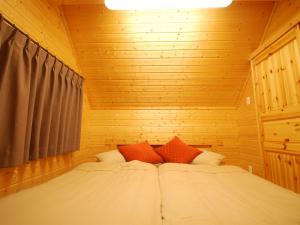 a bed in a wooden room with two red pillows at Cottage All Resort Service / Vacation STAY 8441 in Inawashiro